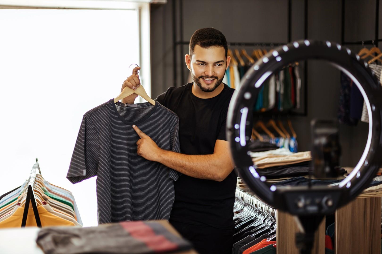 Homem segurando camisa em frente à um smartphone e ring light